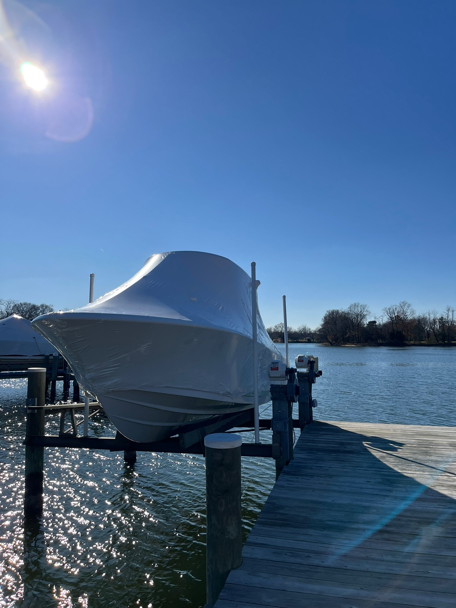 A powerboat under a tight white shrink-wrap cover on a boat lift over the water