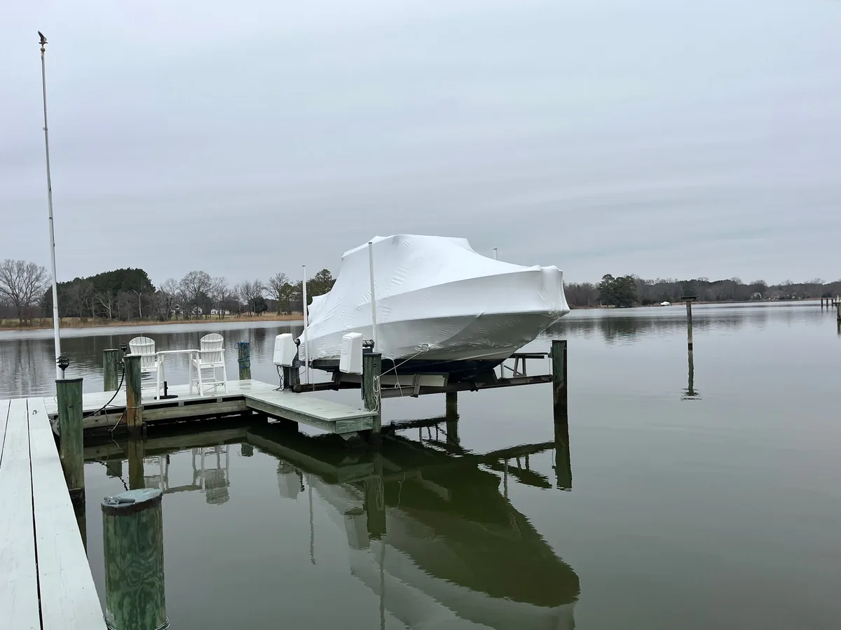 Shrink-wrapped powerboat on a residential lift beside calm water